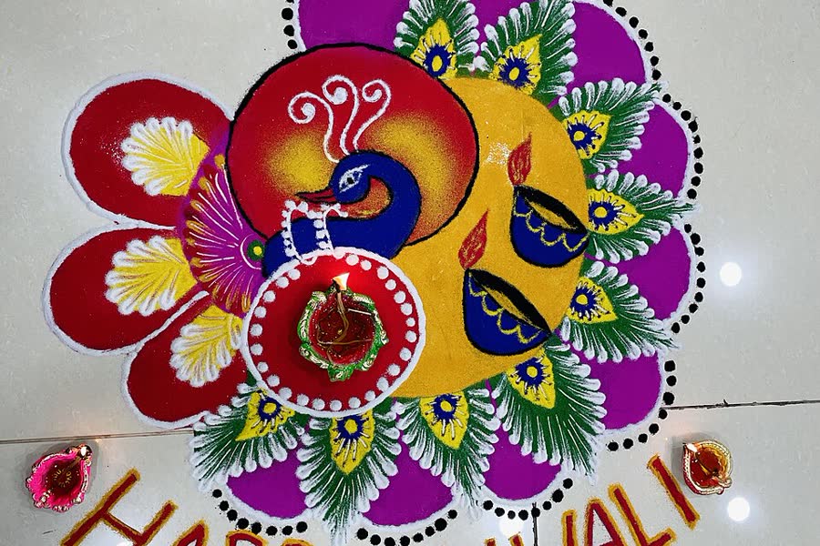 A colourful peacock rangoli with lit clay lamps and the words Happy Diwali