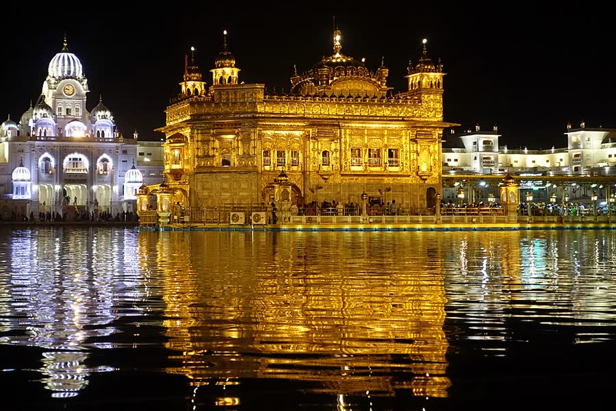The Golden Temple in Amritsar glowing gold at night, reflected in the sacred pool